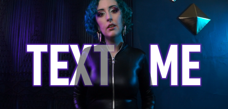 Femdom Findom Goddess Miss Faith Rae stares down at you. She wears a tight shiny wetlook catsuit with a zipper up the front. The lights accentuate the curve of her breasts. Text overlay says, TEXT ME